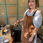 Person wearing a brown apron in a workshop setting with a jewelry making torch.