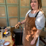 Person wearing a brown apron in a workshop setting with a jewelry making torch.