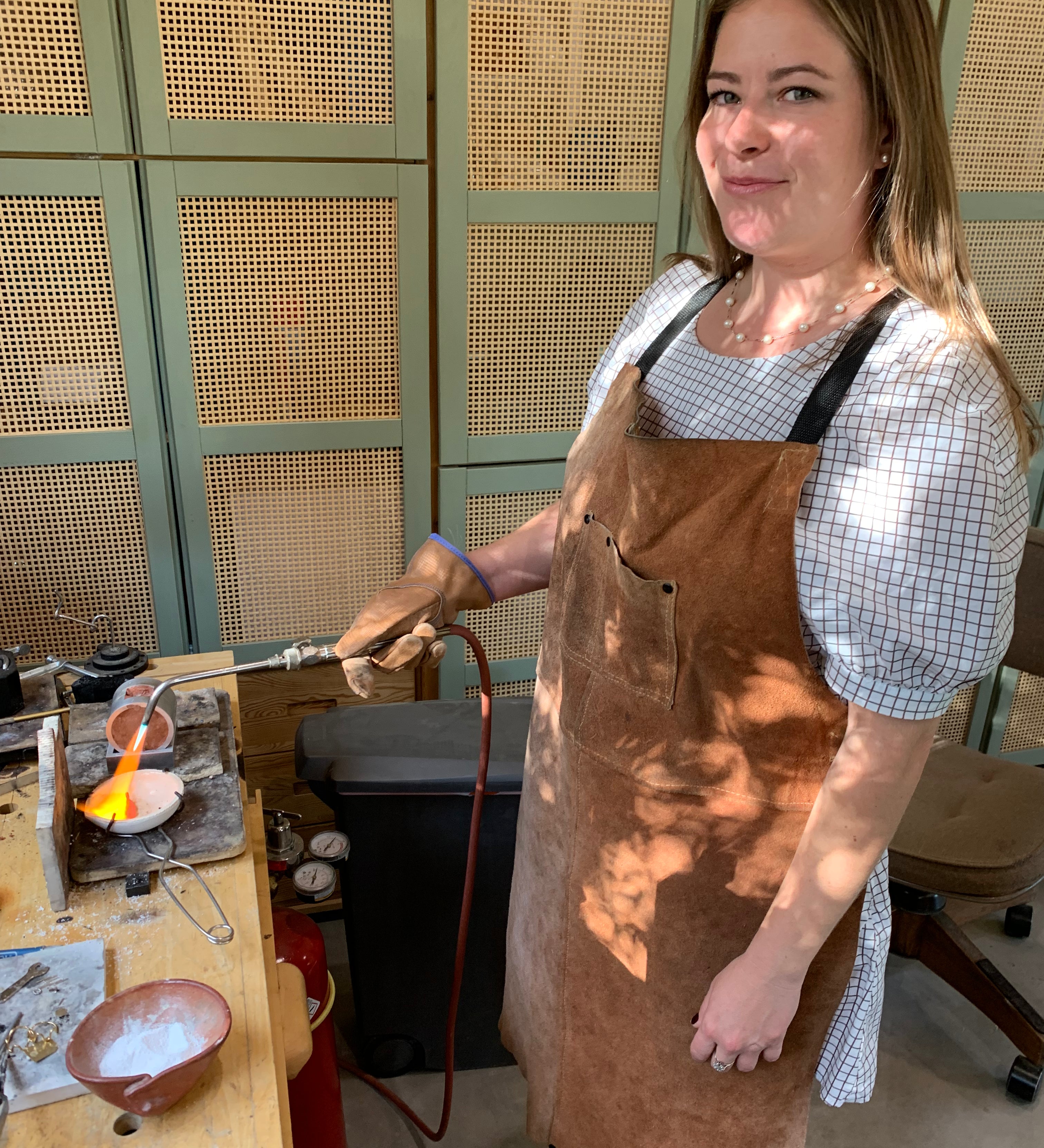Person wearing a brown apron in a workshop setting with a jewelry making torch.
